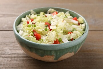 Tasty salad with Chinese cabbage, bell pepper and green onion in bowl on wooden table, closeup