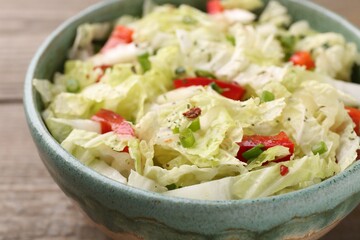 Tasty salad with Chinese cabbage, bell pepper and green onion in bowl on wooden table, closeup