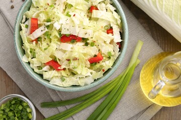 Tasty salad with Chinese cabbage in bowl, oil and green onion on wooden table, flat lay