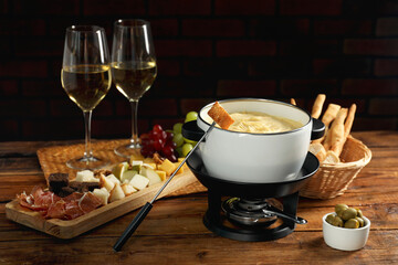 Fondue with tasty melted cheese, forks, different snacks and wine on wooden table