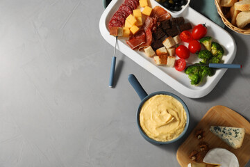 Fondue with tasty melted cheese, forks and different snacks on grey table, flat lay. Space for text