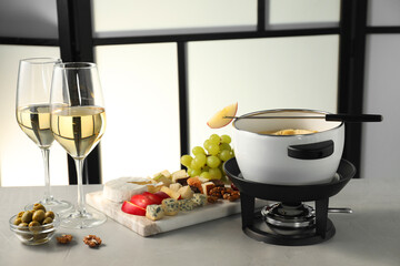 Fork with piece of apple, melted cheese in fondue pot, wine and products on grey table