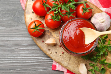 Tasty ketchup, fresh tomatoes, parsley and spices on grey wooden table, flat lay. Space for text