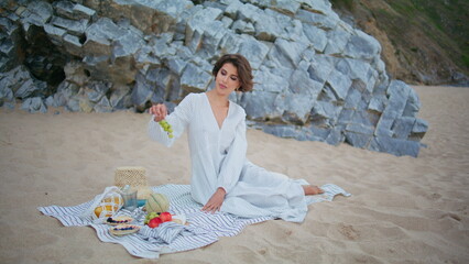 Woman having beach picnic at ocean cliff. Smiling lady holding tasty fruits
