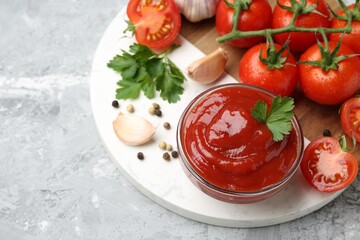 Delicious ketchup in bowl, parsley, garlic and tomatoes on grey textured table, above view. Space for text