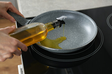 Vegetable fats. Woman pouring cooking oil into frying pan on stove, closeup