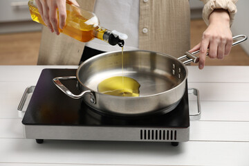 Vegetable fats. Woman pouring cooking oil into frying pan on stove in kitchen, closeup
