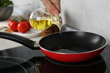 Vegetable fats. Woman pouring cooking oil into frying pan on stove in kitchen, closeup