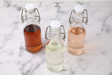 Different types of vinegar in bottles on light marble table, closeup