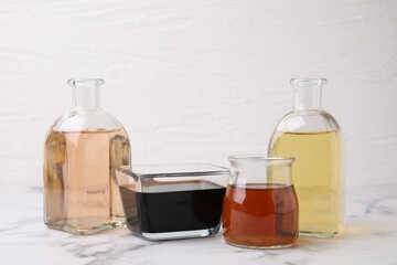 Different types of vinegar on light marble table, closeup