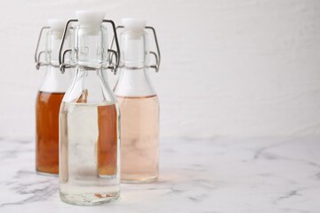 Different types of vinegar in bottles on light marble table, closeup. Space for text