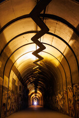 Urban, graffiti-covered tunnel with zigzag installation and warm lights leading to bright exit