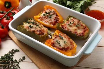 Tasty stuffed peppers in dish and ingredients on wooden table