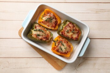 Tasty stuffed peppers in dish on wooden table, top view