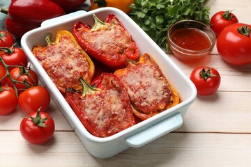 Tasty stuffed peppers in dish and ingredients on light wooden table