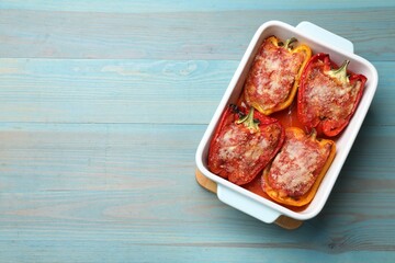 Tasty stuffed peppers in dish on light blue wooden table, top view. Space for text