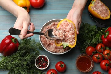 Woman making stuffed peppers with ground meat at light blue wooden table, top view