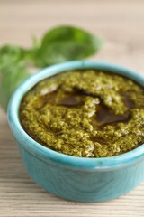 Tasty pesto sauce in bowl and basil on wooden table, closeup