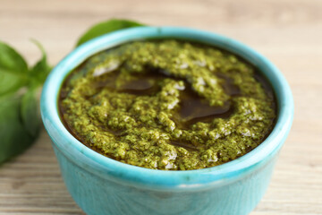 Tasty pesto sauce in bowl and basil on wooden table, closeup