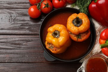 Tasty stuffed peppers in pan, sauce and products on wooden table, flat lay. Space for text