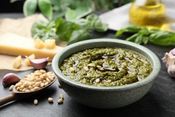 Tasty pesto sauce in bowl, pine nuts and garlic on black table, closeup