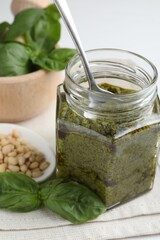 Tasty pesto sauce in glass jar, spoon, pine nuts and basil on table
