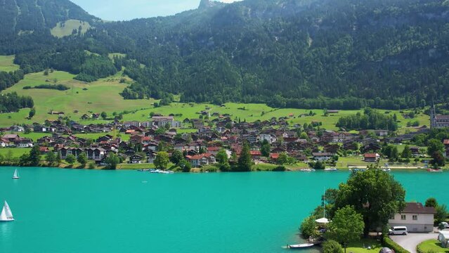 Drone footage of turquoise clear lake Lungern or Lungerersee in Switzerland in summer sunny day with village and green meadow