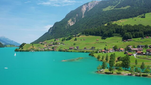 Drone footage of turquoise clear lake Lungern or Lungerersee in Switzerland in summer sunny day with village and green meadow