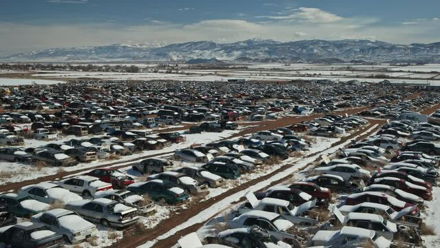 Aerial flyover view of rows of salvage cars in junkyard near mountain range / Aurora, Utah, United States