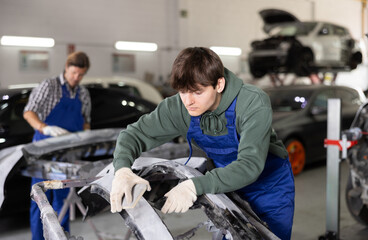 Young guy mechanic in uniform polishes part of car with sponge in car service station