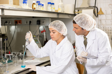 Focused male and female chemist pipetting blue reagent into solution in test tube and taking notes...
