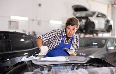 Man prepares car for painting in workshop - grinds and puts putty on the bumper before painting