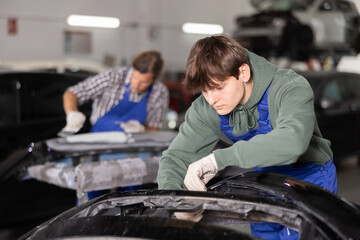 Fototapeta na wymiar Young guy mechanic in uniform repairs car part in car service station