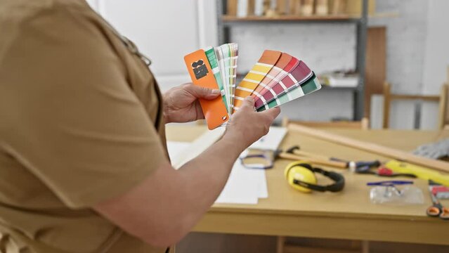 A man in a carpentry workshop holds color swatches, indicating choices for a woodwork project.