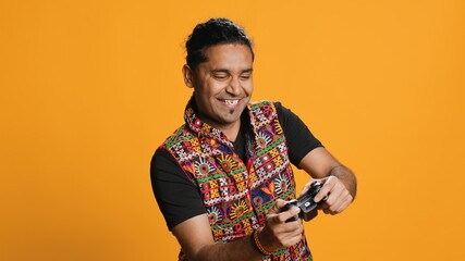 Happy gamer celebrating after winning game on gaming console, studio background. Delighted Indian...