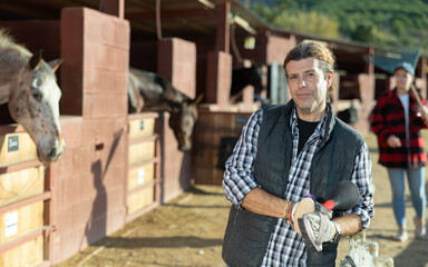 Portrait of owner of horse farm against the background of a stall with horses