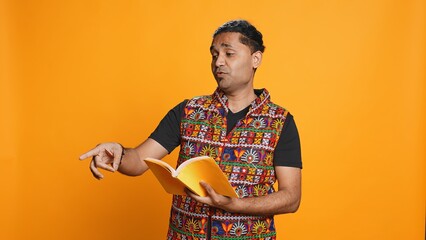 Joyous indian teacher reading book for pupils during class, isolated over studio background....