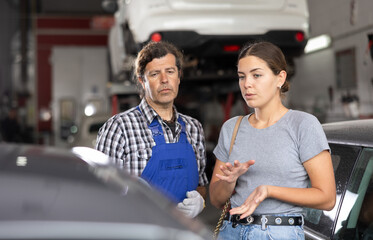 Expert mechanic providing detailed explanation to interested young female car owner regarding...