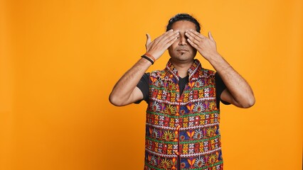 Man wearing traditional indian clothing covering eyes, ears and mouth, imitating three wise...
