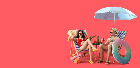 Young couple with strawberries in deck chairs and beach accessories on red background