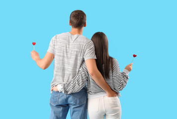 Happy young couple with hearts on blue background, back view