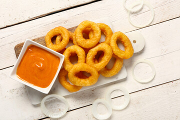 Board with fried breaded onion rings and sauce on white wooden background