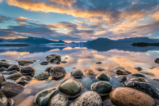 Light beam of golden cloud atmosphere over Lake Te Anau, in the back mountain ranges of the Stuart Mountains and Franklin Mountains, in the front round stones, Fjordland National Park, Te Anau, Te