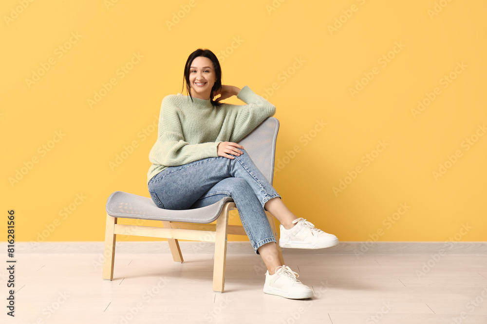 Wall mural beautiful young woman resting in comfortable chair near yellow wall