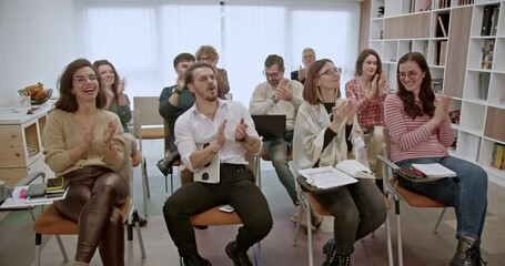 In a contemporary classroom setting, a cross-generational business team is clapping hands in a seminar, demonstrating unity and appreciation for the shared learning experience.