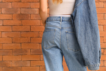 Young woman in stylish jeans clothes near orange brick wall, back view