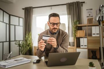 Adult businessman buy online on laptop and hold credit card at office