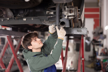 Young mechanic is repairing a car - changing the shock absorber of the car rear suspension