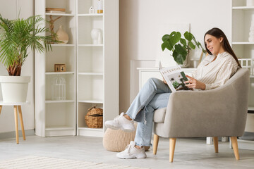 Beautiful woman reading magazine in armchair at home