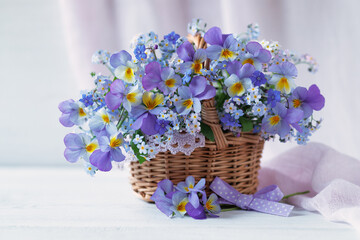 Spring forget-me-not flowers, viola pansy in a basket, bouquet with ribbon on a white table.